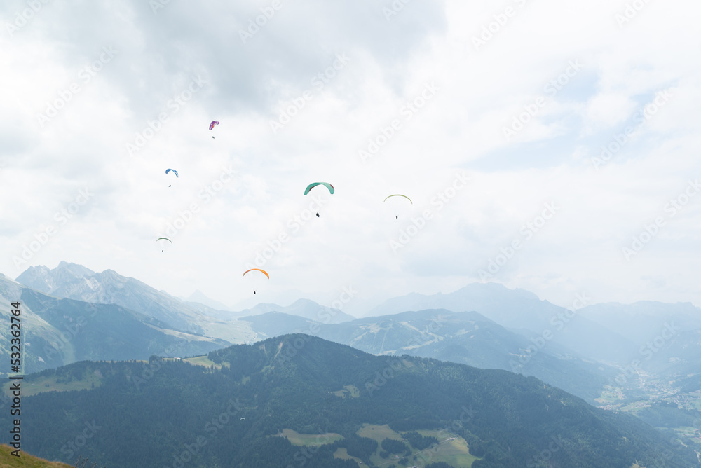 A paraglider group flying over mountain peaks on a cloudy day at french alps. A paraglider group flying over mountain peaks on a cloudy day at french alps.