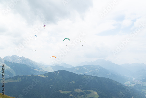 A paraglider group flying over mountain peaks on a cloudy day at french alps. 