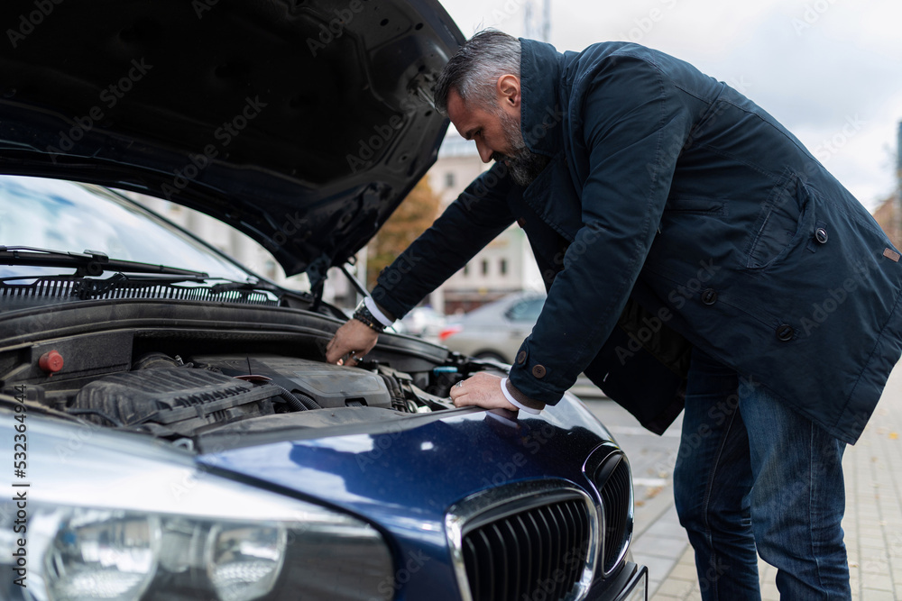 a man checks the technical condition of the car before the trip, bending over the hood and engine a man checks the technical condition of the car before the trip, bending over the hood and engine
