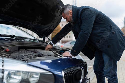 a man checks the technical condition of the car before the trip, bending over the hood and engine