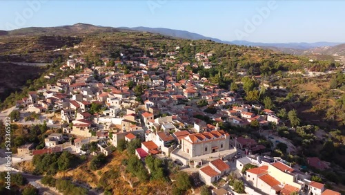 Aerial drone sunset footage of traditional countryside hilltop village Vouni, in Limassol, Cyprus. 360 view of christian church Ioannis Prodromos, ceramic tiled roof houses, narrow streets from above. photo