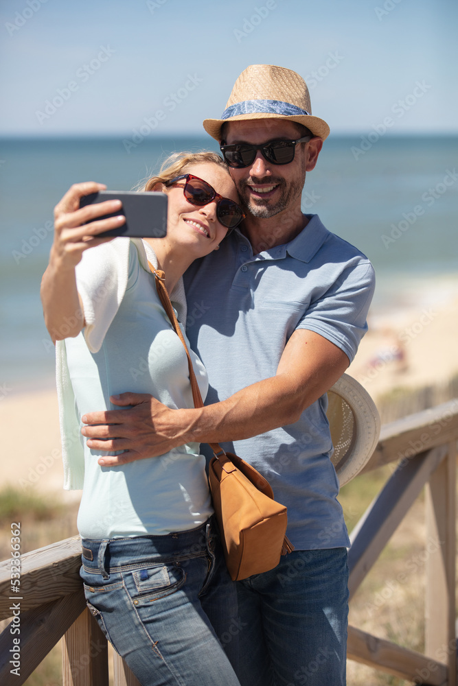 happy couple taking selfie at beach during sunny day