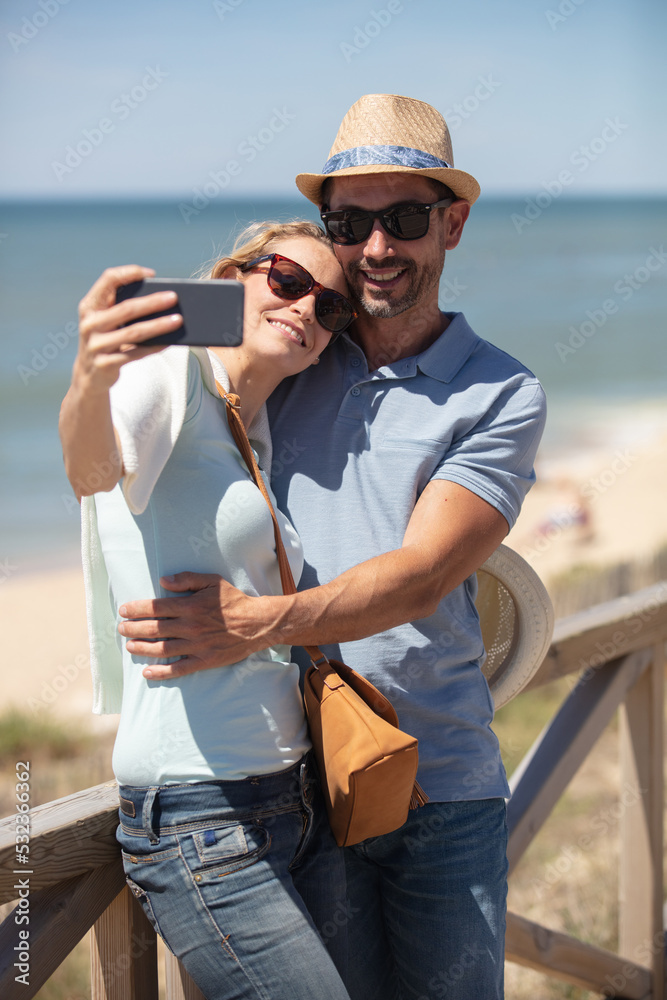 happy couple taking selfie at beach during sunny day happy couple taking selfie at beach during sunny day