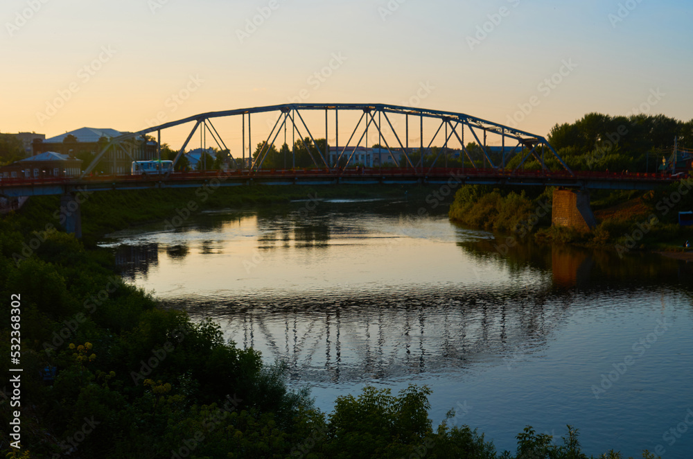 View of small steel bridge over the river or lake with dense coniferous forest on background