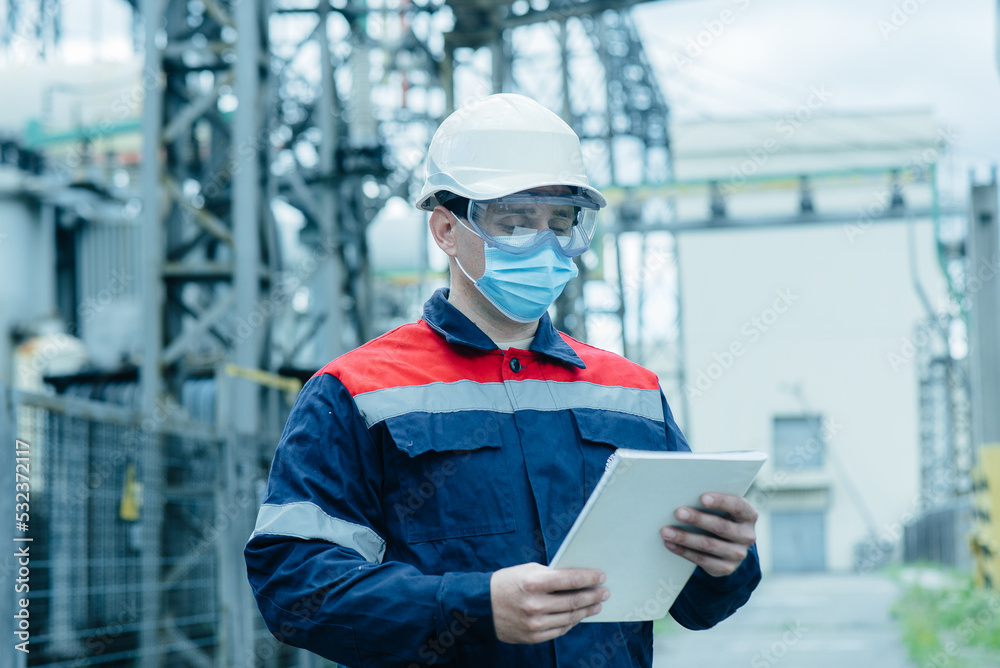 A masked power engineer during a pandemic inspects the modern equipment of an electrical substation before commissioning. Energy and industry. Scheduled repair of electrical equipment. A masked power engineer during a pandemic inspects the modern equipment of an electrical substation before commissioning. Energy and industry. Scheduled repair of electrical equipment.