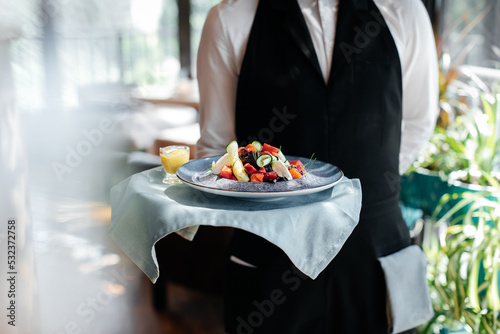 Wallpaper Mural Close-up of a young waiter in a stylish uniform carrying an exquisite salad to a client in a beautiful gourmet restaurant. Table service in the restaurant. Torontodigital.ca