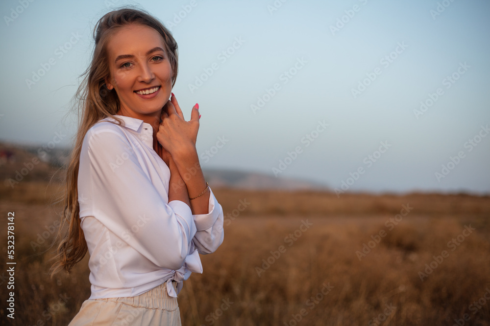 Beautiful woman with natural blond hairs posing in the nature against  the field with dry grass and sky