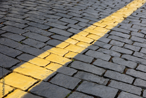 Stone pavement texture, cobbled street. Road marking, yellow line on tiles