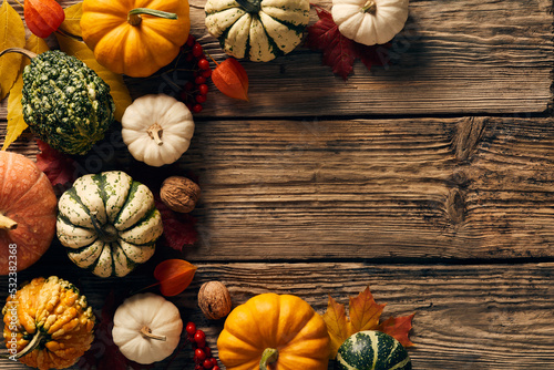 Autumn frame made of pumpkins, fall leaves, red berries, walnuts on wooden table. Happy Thanksgiving Day concept. Flat lay, top view, copy space.