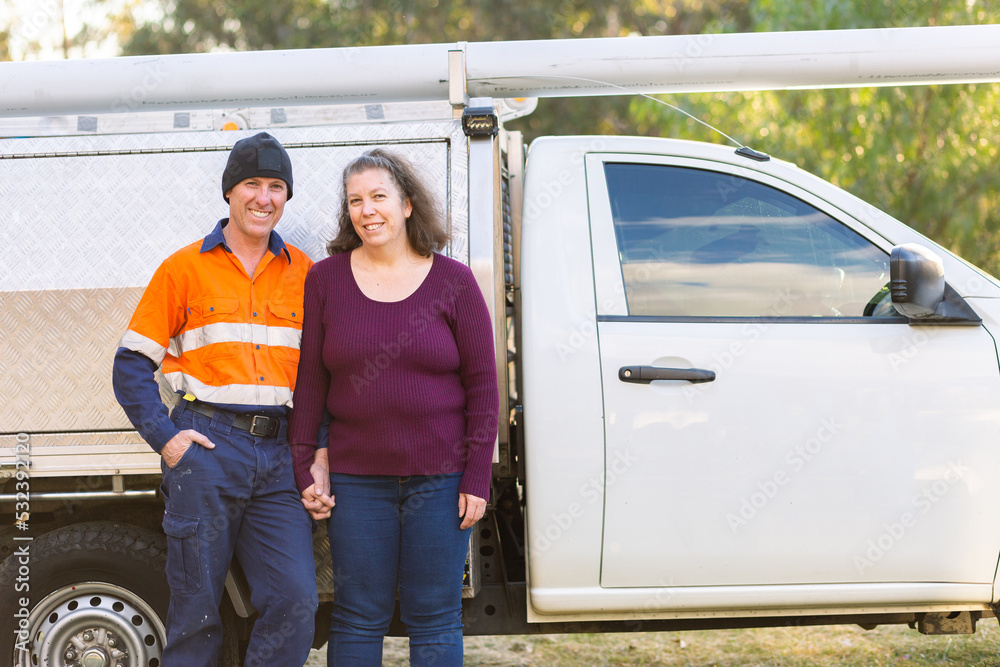 happy middle age couple standing together in front of tradie work ute happy middle age couple standing together in front of tradie work ute