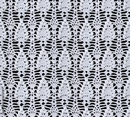 Seamless knitted texture. This beautiful floral pattern is crocheted with white threads. Cotton yarn. White lace on a black background.