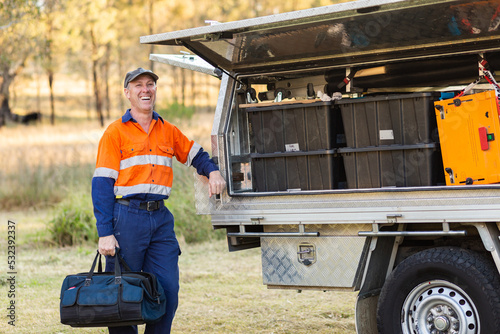 Happy male handyman with toolbox bag laughing near tradie ute