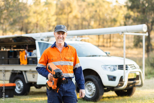 Handyman with nail gun power tool beside tradie ute