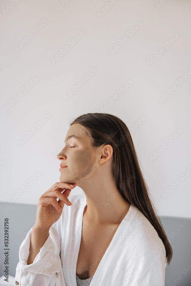 Portrait of young caucasian woman with brunette hair gently touched face, closed eyes at home. Calm girl sitting on bed and enjoying life. Concept lifestyle, beauty procedures. Portrait of young caucasian woman with brunette hair gently touched face, closed eyes at home. Calm girl sitting on bed and enjoying life. Concept lifestyle, beauty procedures.