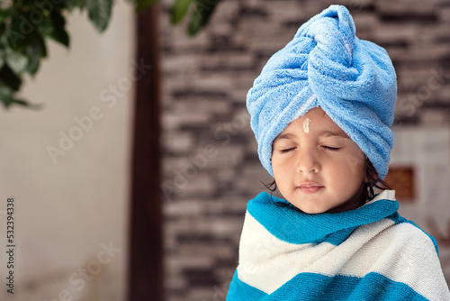 Obraz na plátně 22 months old cute  Indian baby girl wearing blue Hair Towel Wrap Turban and body wrapped with blue and white towel, sandalwood anoint on her forehead sitting with eyes closed smiling expressions