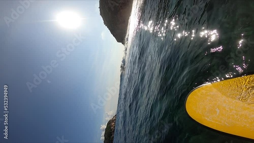 Bright sun reflects on ocean water while person surfing, vertical POV slow motion