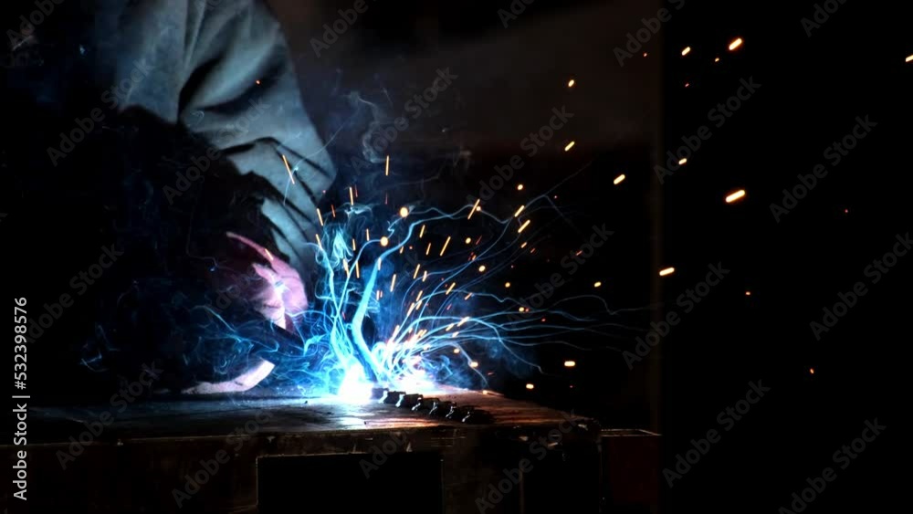 Factory worker welds metal. The man is welding. Welding with argon or electrode, using a welding machine. An industrial enterprise producing metal structures. Sparks and flashes fly. Slow motion Factory worker welds metal. The man is welding. Welding with argon or electrode, using a welding machine. An industrial enterprise producing metal structures. Sparks and flashes fly. Slow motion