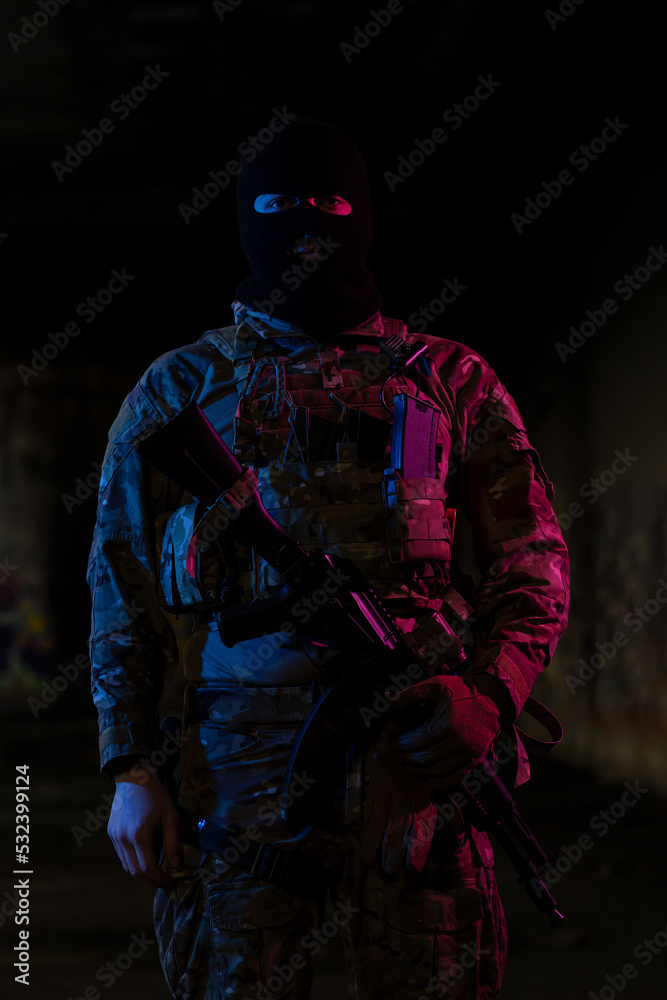 Army soldier in Combat Uniforms with an assault rifle and combat helmet night mission dark background. Blue and purple gel light effect. 