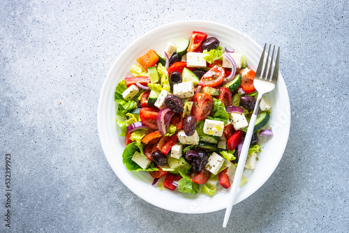 Greek salad with olives, feta cheese and fresh vegetables. Top view on light stone table.