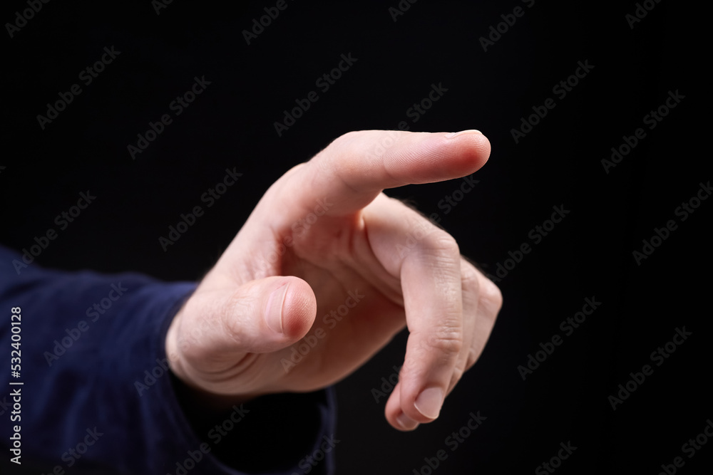 The finger of a male hand points to something on a dark background