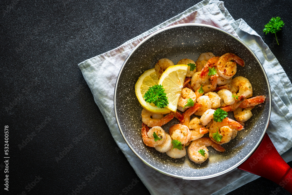 Frying shrimps with lemon in the frying pan. Top view image on black. Frying shrimps with lemon in the frying pan. Top view image on black.