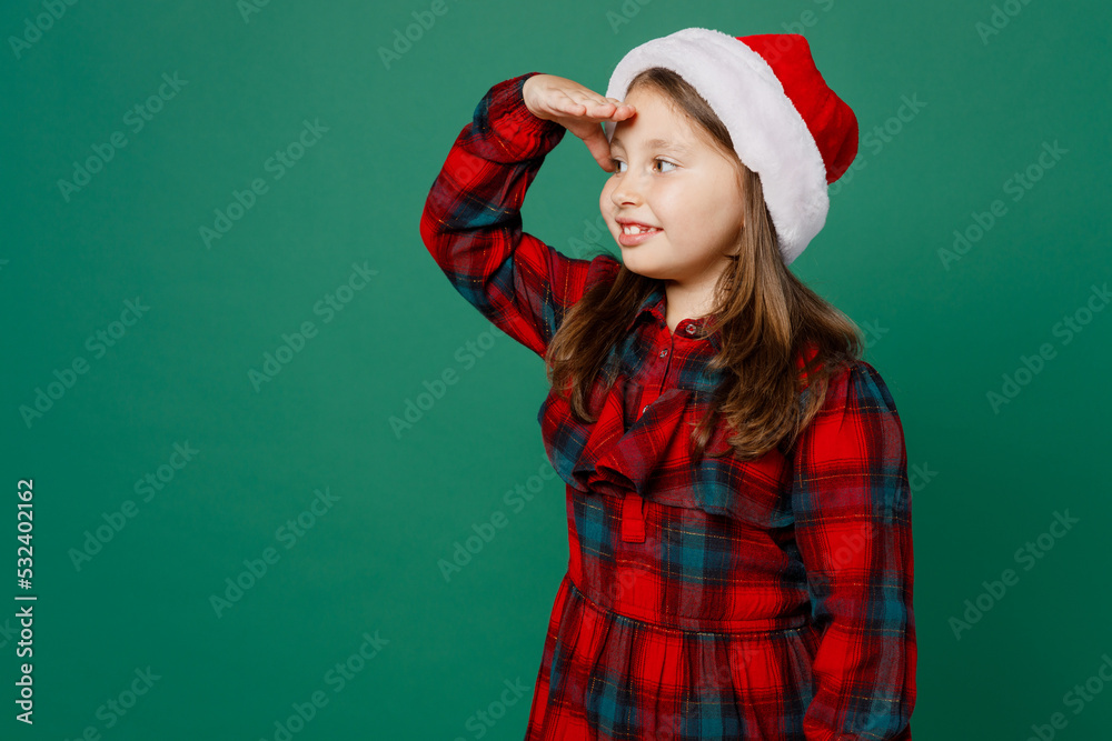 Side view merry little child kid girl 6-7 year old in red dress Christmas hat posing hold hand at forehead look far away distance isolated on plain dark green background. Happy New Year 2023 concept Side view merry little child kid girl 6-7 year old in red dress Christmas hat posing hold hand at forehead look far away distance isolated on plain dark green background. Happy New Year 2023 concept