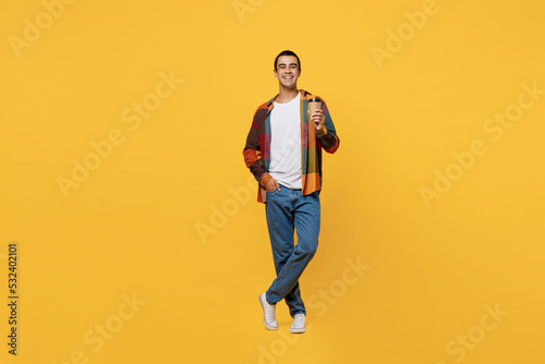 Full body young middle eastern man 20s he wear casual shirt white t-shirt hold takeaway delivery craft paper brown cup coffee to go isolated on plain yellow background studio People lifestyle concept.