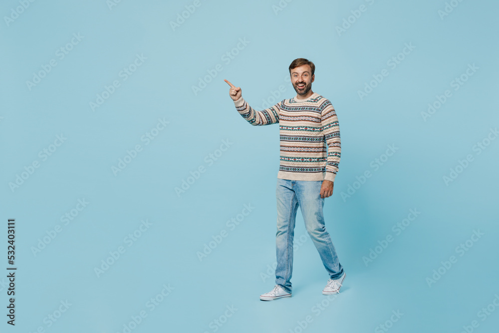 Full body young smiling happy cheerful man 30s he wears sweater walking going point index finger aside on workspace area isolated on plain pastel light blue cyan background. People lifestyle concept.