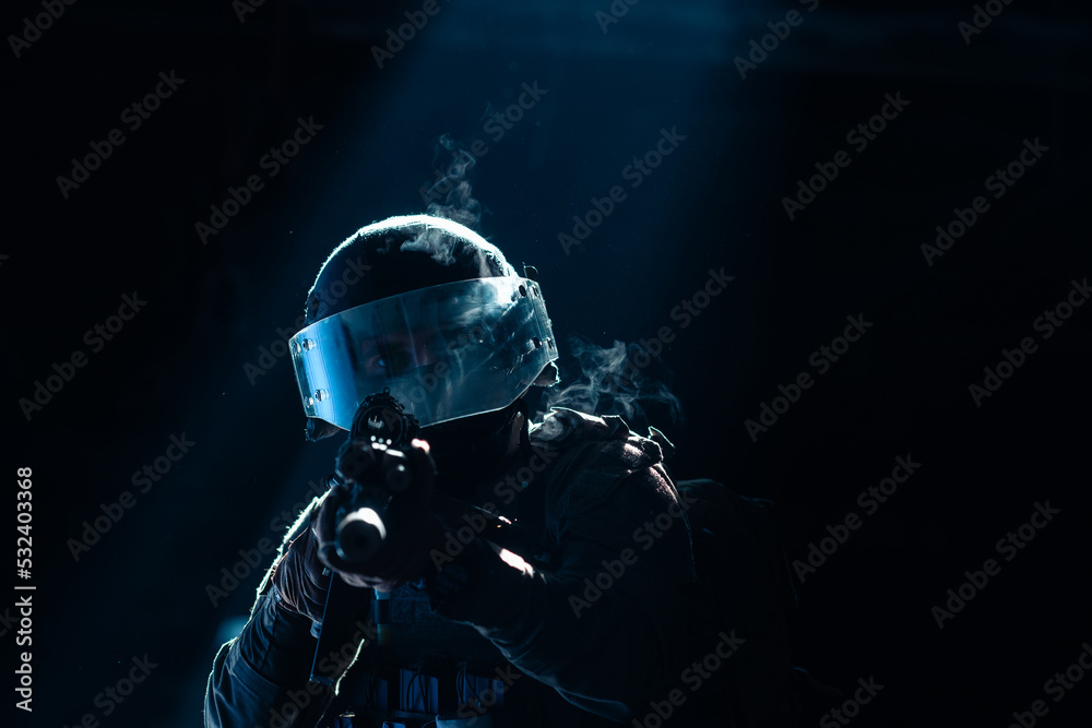 Army soldier in Combat Uniforms with an assault rifle and combat helmet night mission dark background. Blue and purple gel light effect. 