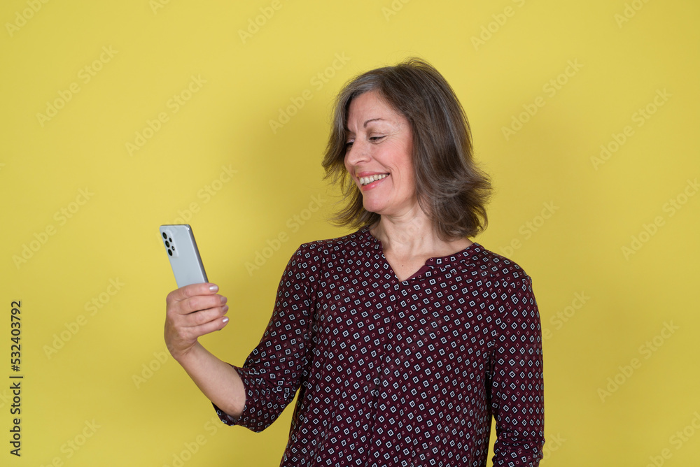 Mature woman using smart phone on yellow wall Mature woman using smart phone on yellow wall