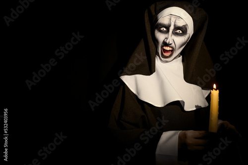 Obraz na płótnie Scary devilish nun with burning candle on black background, space for text