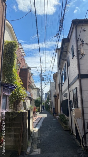 The narrow street of Tokyo, Nezu district year 2022 on a sunny day with clouds, street wires and varieties of retro houses