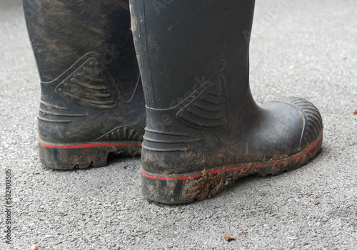Dirty black rubber boot soles. Dirt is stuck to them. The boots are standing on a tarmac floor.
