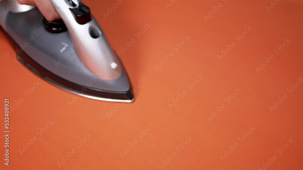 Female Hand Ironing a Bright Orange Cloth with a Steam Iron on an