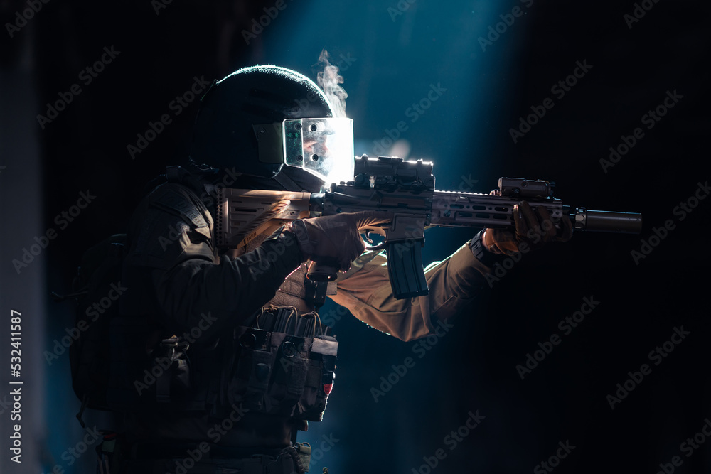 Army soldier in Combat Uniforms with an assault rifle and combat helmet night mission dark background. Blue and purple gel light effect. Army soldier in Combat Uniforms with an assault rifle and combat helmet night mission dark background. Blue and purple gel light effect.