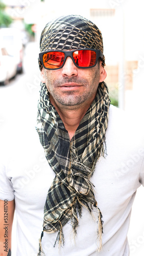 Hombre Joven con pañuelo en la cabeza y gafas, pañuelo tipo  árabe, shemag, pirata, o bandolero, sonriendo a cámara. photo