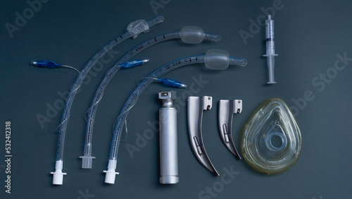 tracheal intubation kit: laryngoscope, several laryngoscope blades and several endotracheal tubes, a syringe to inflate the cuff of the tube. on a dark background, close-up photo