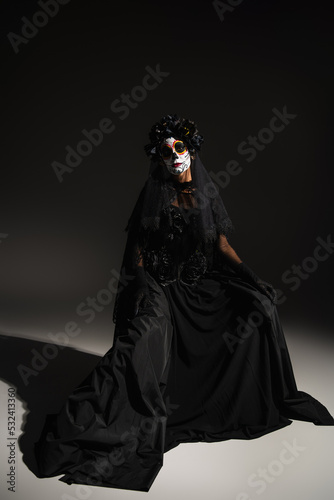 full length of woman in black dress and with spooky halloween makeup on dark background.