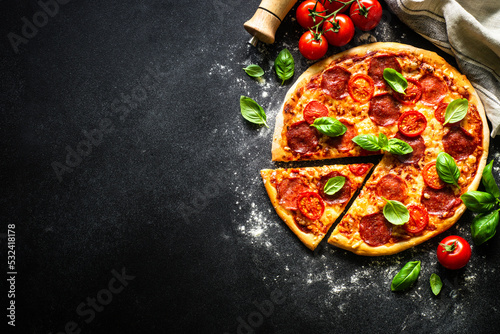 Pizza with salami cheese, tomatoes and basil on black table. Top view with copy space, macro.