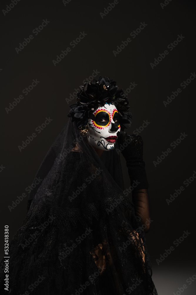 woman in spooky halloween makeup and black wreath with veil looking at camera on dark background. - obrazy, fototapety, plakaty 