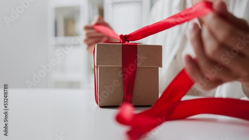 Female hands open unpack gift gift box red ribbon bow on a gift box on a holiday. Gentle scene of opening a gift on a light background. gift for valentine's day new year birthday wedding anniversary
