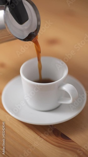 Pouring coffee from a Italian coffee machine to a small white coffee cup Vertical video photo