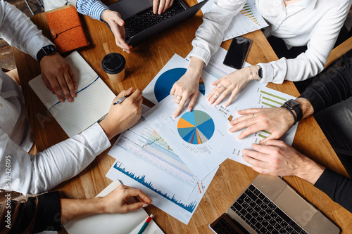 Top view on graphs and charts, laptop and hands of employees on the table. There is a discussion. their faces are not visible