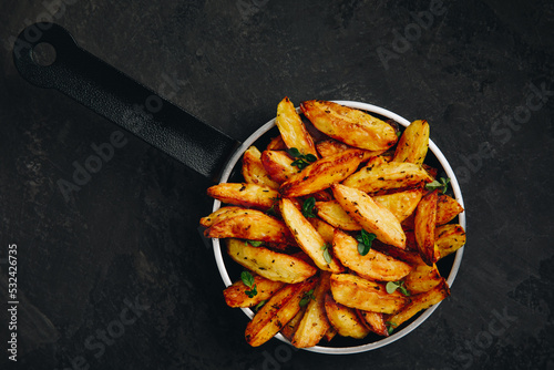 Roasted potatoes. Baked potato wedges in frying pan on dark stone background.