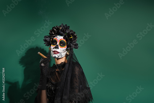 Woman in day of death halloween costume holding cigar on green background.