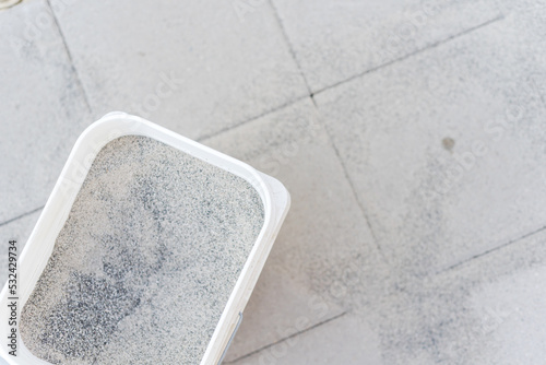 A full bucket of polymeric paver sand on top of gray concrete patio stone paver walkway