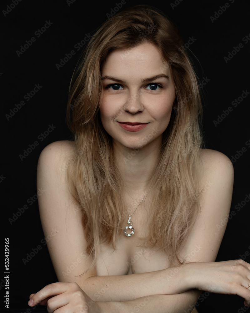 Vertical portrait of positive, confident, delightful young naked blonde woman with necklace in black studio. Waist up Vertical portrait of positive, confident, delightful young naked blonde woman with necklace in black studio. Waist up