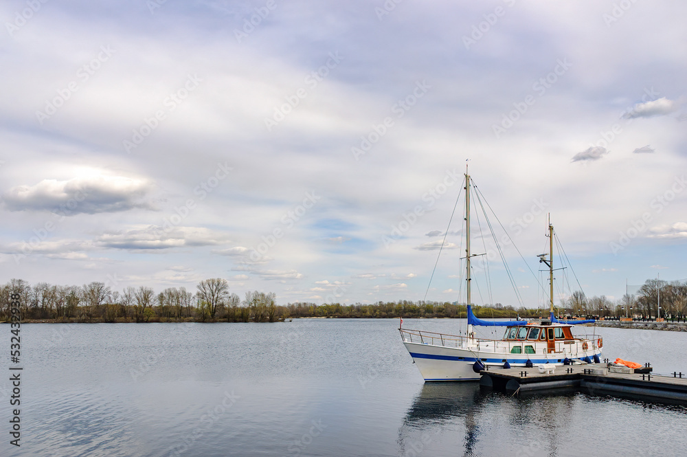 Fototapeta premium A wooden sailboat moored at a pontoon in the Obolon district, on the Dnieper River in Kiev, Ukraine, under a beautiful blue and cloudy sky, during the hot summer days.