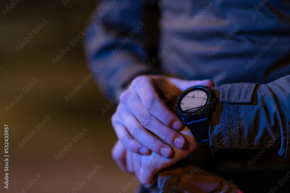Modern warfare soldier checking navigation, time and other information on a smartwatch. Dark night black background. Modern warfare soldier checking navigation, time and other information on a smartwatch. Dark night black background.