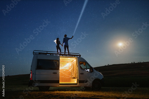 a couple standing on a mobile home with a flashlight with a starry night sky background